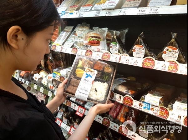 고객이 이마트24 맛보장 홍보물이 붙어 있는 프레시 푸드 매대에서 맛보장 도시락을 살펴보고 있다.